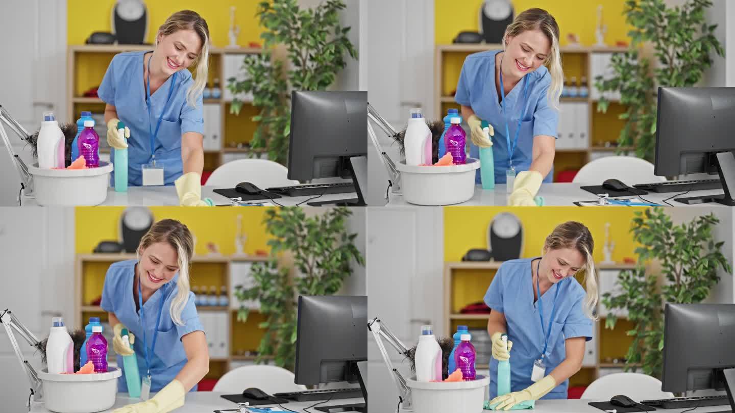 年轻的金发女专业清洁工在办公室微笑着打扫桌子
