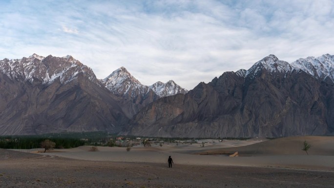 在巴基斯坦北部斯卡都的喀喇昆仑山脉，寒冷的沙漠，周围有雪帽山，移动的云和灰尘吹过沙丘