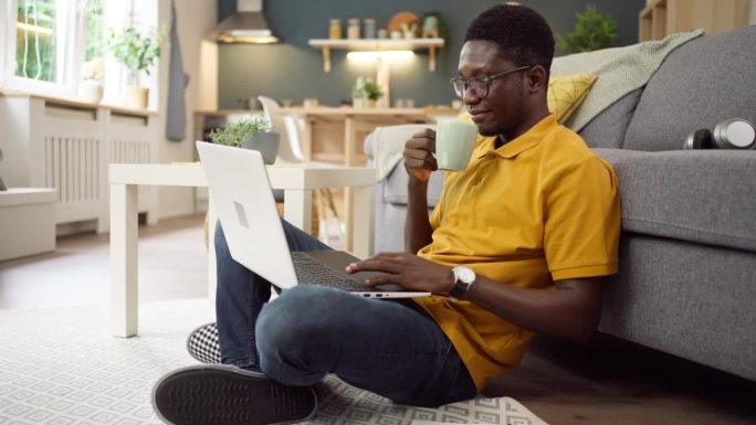 非裔美国人一边喝咖啡，一边在家用笔记本电脑工作