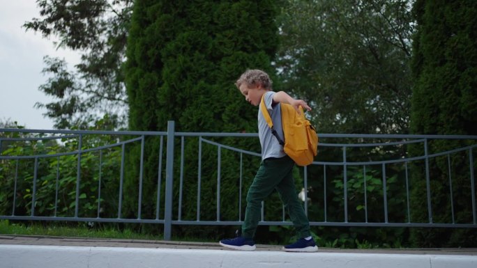 无忧无虑的男孩放学后在公园散步，背着背包的孩子在路边保持平衡
