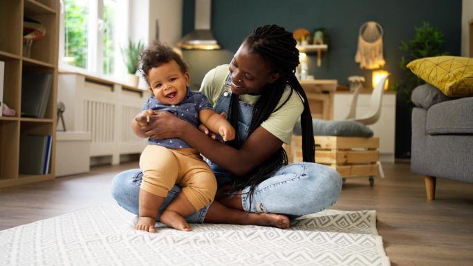 快乐的母亲和婴儿黑人在家里玩耍