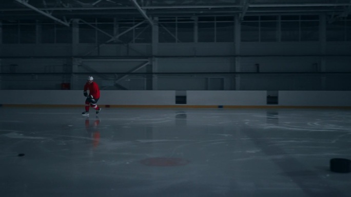 一段快节奏的视频，一名曲棍球运动员在黑暗的冰场上训练，避开障碍物，向守门员进球
