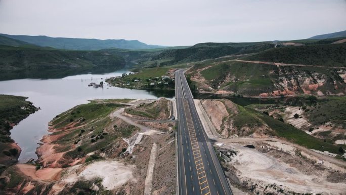 美丽的多车道公路，黄色的标志和横跨湖的桥梁在山和绿色的森林。无人机航拍图