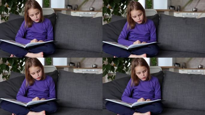 一个可爱的金发小女孩正坐在客厅的沙发上读一本彩色的大书。低龄学童自学，在家阅读文学作品，趣味休闲
