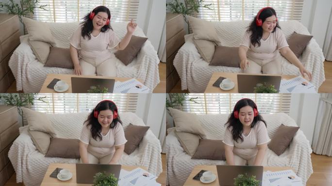 身材魁梧、头戴红色耳机的年轻女子正心情愉快地坐在笔记本电脑前工作，跳着轻快的舞蹈。在客厅里有百叶窗的
