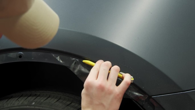将PPF保护膜涂在汽车上的过程。工人正在给一辆黑色轿车涂保护膜。特写镜头