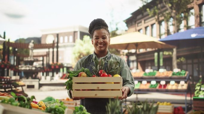 一个黑人女性在农贸市场的摊位上与新鲜的有机农产品工作的肖像。非洲女商人拿着装满水果和蔬菜的板条箱，微