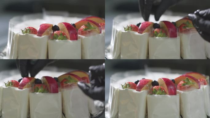 一个戴着黑色手套的厨师的手在蛋糕上把苹果片、蓝莓片和草莓片围成一个圈。装饰蛋糕。