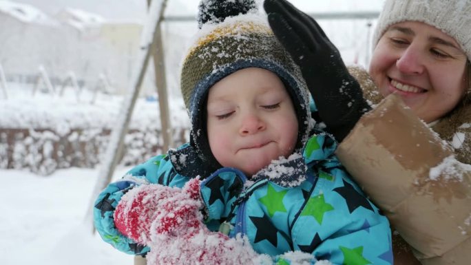 年轻有爱心的母亲在公园玩耍后，为儿子抖掉身上的雪。寒假里的欢乐，孩子们在户外玩耍，在雪中活动