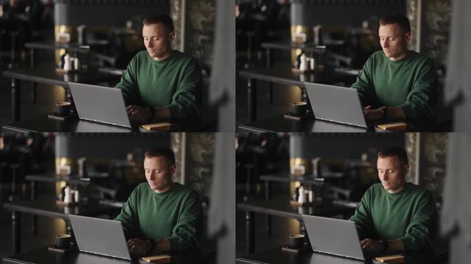 黑客或程序员在网上用笔记本电脑工作，男人独自坐在咖啡馆的桌子旁