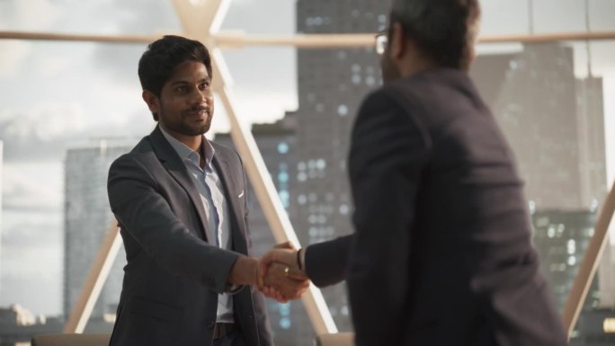 年轻的印度商人在公司现代化办公室的会议室里完成一笔生意。两个穿着经典西装的男人握手庆祝成功的伙伴关系