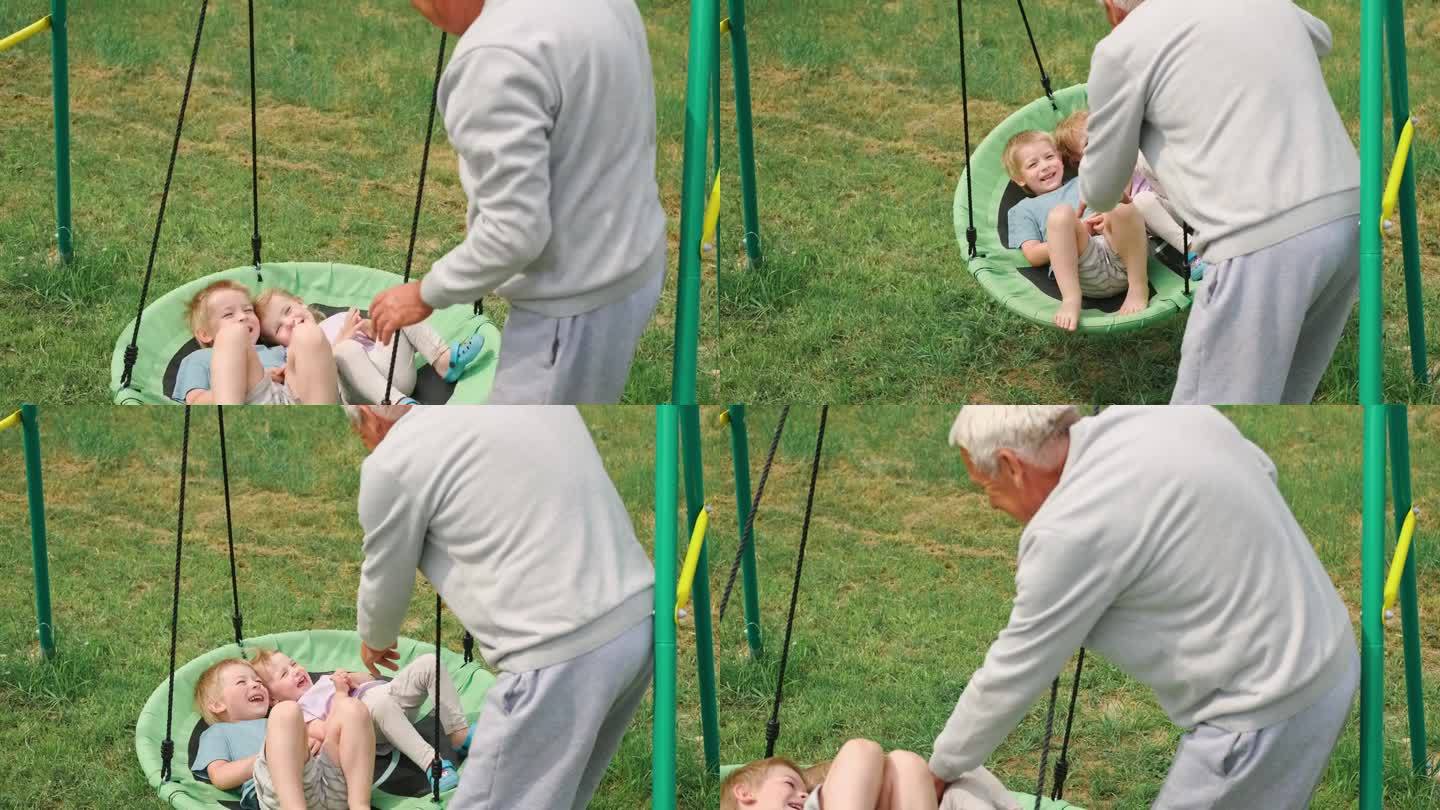爷爷在夏日公园里荡秋千。爷爷和孙子们坐在户外秋千上。60多岁的老人在跷跷板上推着小孙子。老人和小孩子