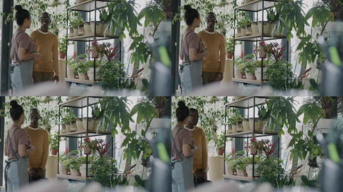 友好的女售货员系着围裙，在花店里向顾客展示室内的植物