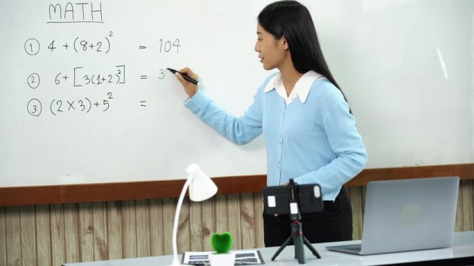 老师一边讲解黑板上的数字，一边与在线学习的学生进行视频通话。