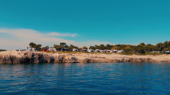 蓝蓝的天空下，平静的海面旁的露营地停着岩石海岸和房车
