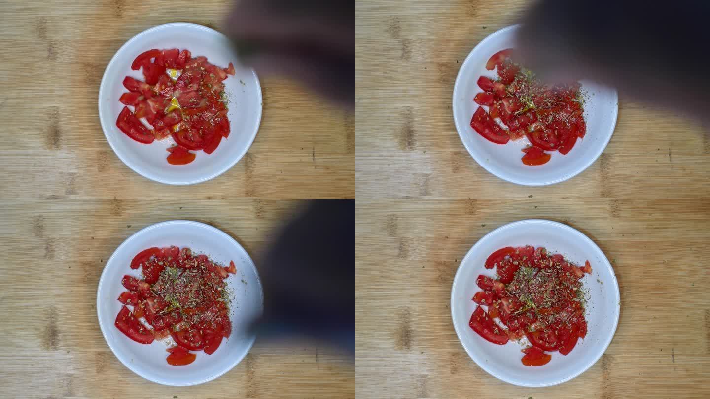 表格，俯视图，POV:一个人在一碗用橄榄油调味的西红柿中加入牛至。将牛至浇在拌有橄榄油的番茄沙拉上。