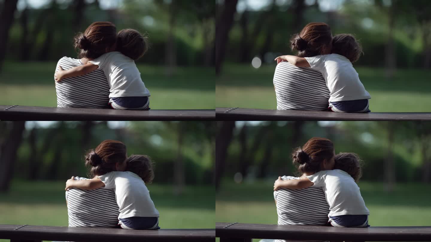 孩子抱着母亲的背影一起坐在公园里。小男孩拥抱妈妈。母爱和关怀理念。儿子和父母