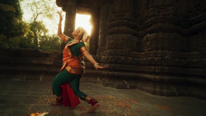穿着传统服装的印度妇女看着镜头，穿着五颜六色的纱丽跳舞的动态镜头。富有表现力的年轻女性在庙里表演民间