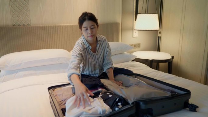 亚洲女背包客为旅行准备衣服和行李旅行箱。