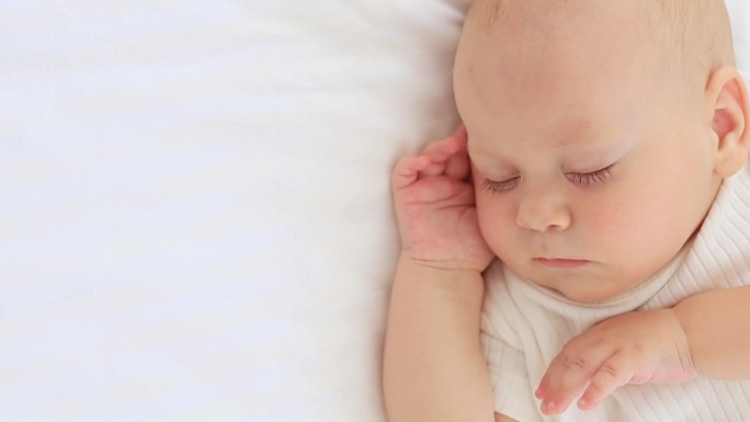 可爱的小新生儿睡觉，他的手交叉在他的脸颊，甜蜜的健康的婴儿睡在一个白色的婴儿床，一个地方的文字