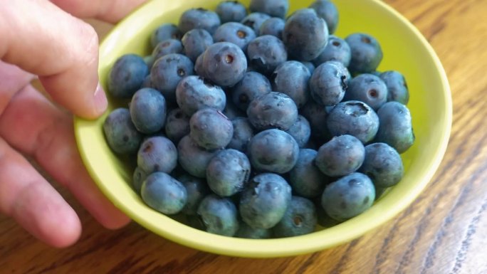 蓝莓在碗里。那只手把一盘浆果放在桌子上。新鲜的蓝莓。吃健康食品的镜头。获得维生素。4 k的视频。