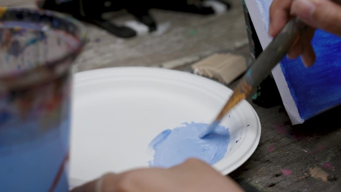 特写笔刷在手上，画家正用长柄笔刷，将藏青色和白色混合在一起，以淡色调变成亮蓝色，亮色的油漆颜色天空，