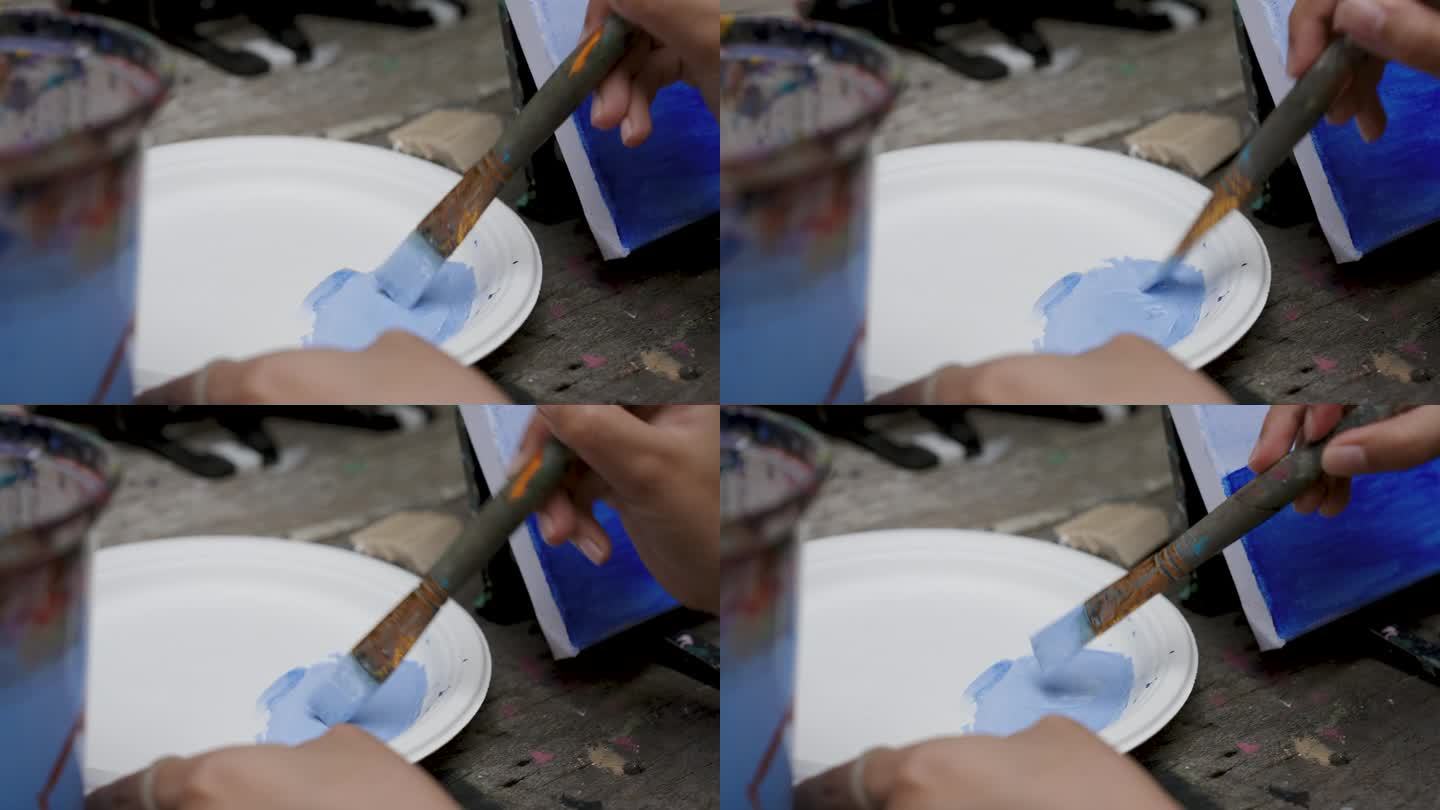 特写笔刷在手上，画家正用长柄笔刷，将藏青色和白色混合在一起，以淡色调变成亮蓝色，亮色的油漆颜色天空，