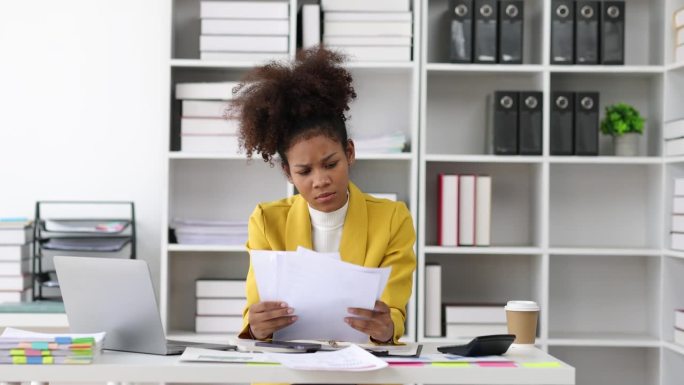 严肃的非裔美国女商人在办公室里忙于文书工作。阅读财务账单和发票的压力大的女人。