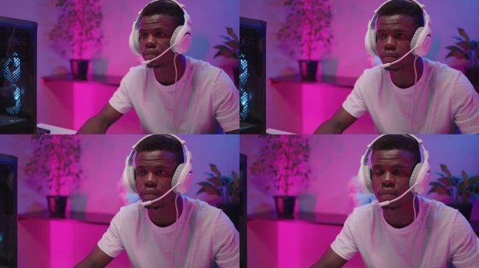 年轻的黑人男性玩家带着耳机独自坐在粉红色霓虹灯的房间里