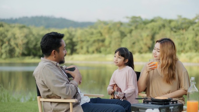 度假时，一个亚洲家庭在草地的野餐桌上玩着尤克里里琴。