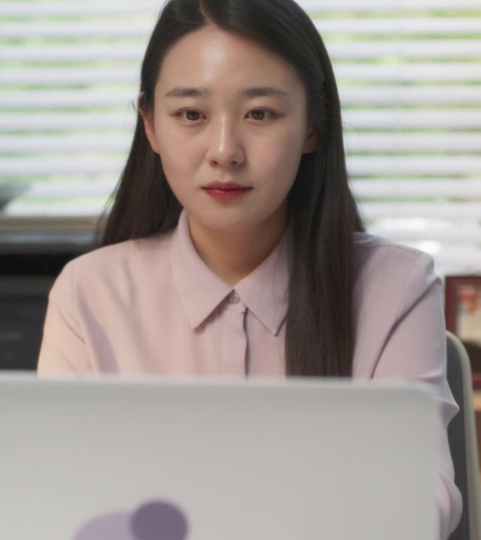 垂直屏幕:美丽的韩国女性在一家时尚创意机构的办公桌后对着电脑工作。年轻快乐的女人合上她的笔记本电脑，