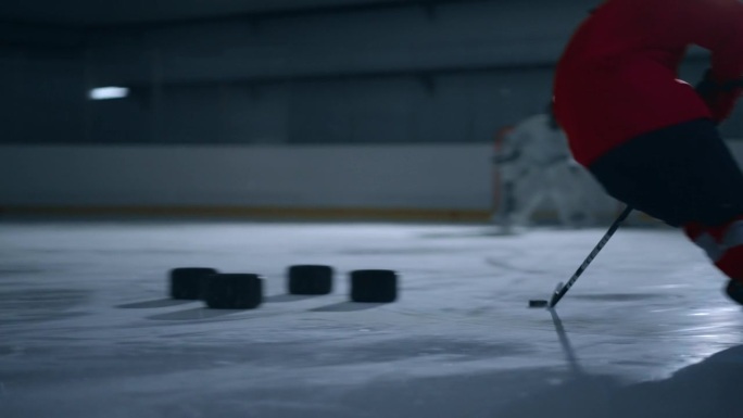 一名身穿红色运动衫的冰球运动员在溜冰场上努力训练的动态画面，他动作迅速，准确地避开了障碍物