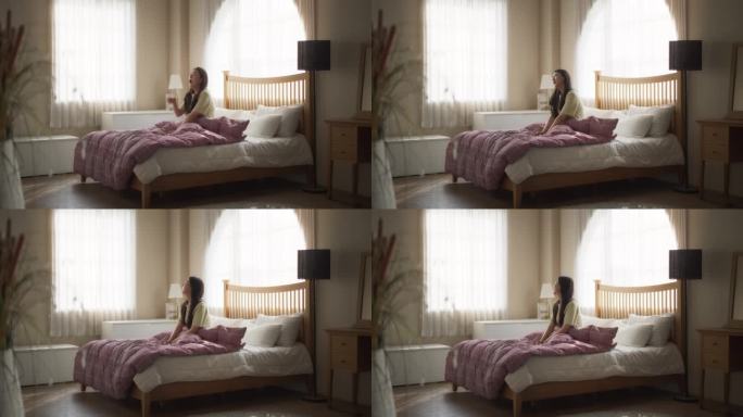 美丽的年轻亚洲女人早上醒来，伸展她的脖子，阳光从公寓的窗户照进卧室。韩国女孩准备好迎接商业机会和新的