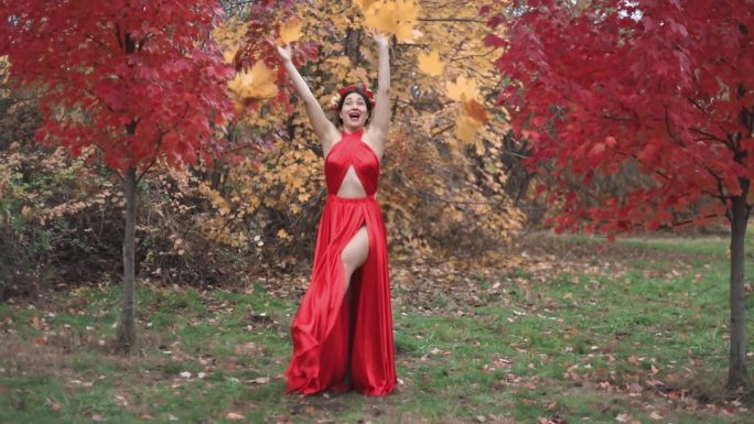 一位女士身穿红裙子，头上戴着花环，抛撒着树叶，在秋天快乐。秋天公园里的女孩。