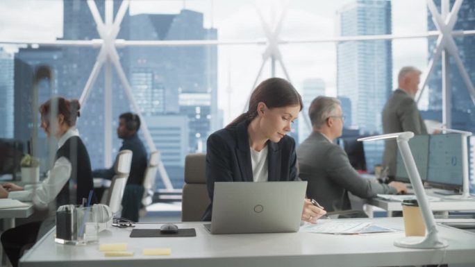 在市中心明亮的摩天大楼办公室里，职业女性业务发展经理在笔记本电脑上打字。成功的白人女性在多样化的工作