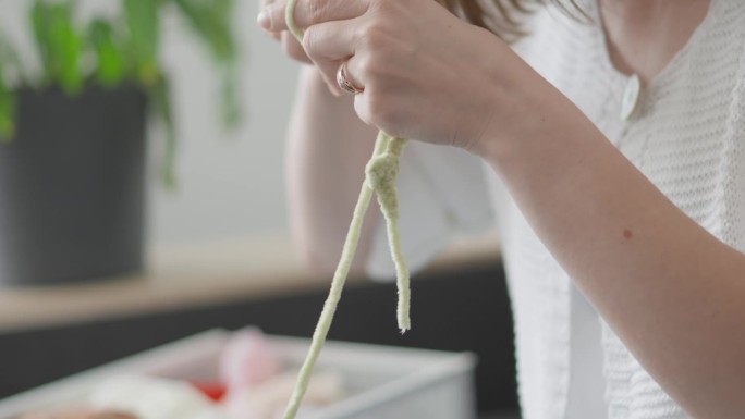 细心的女针线匠专注于编织纱线，熟练地包裹一个钩子，创造出独特的amigurumi软玩具，将成为孩子们