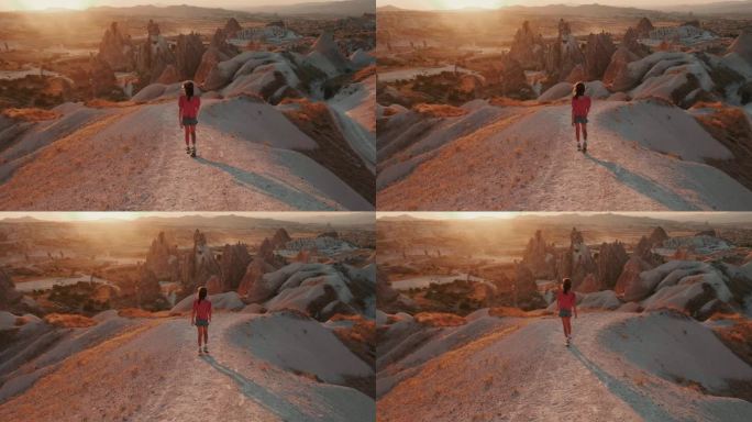快乐的十几岁的女孩走下巨大的岩石悬崖路径享受山景度假在夏日日落卡帕多西亚。