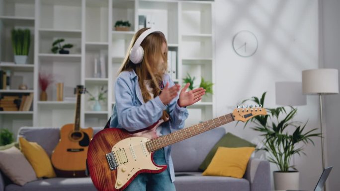 活泼有趣的长发女孩在家里的客厅里弹着电吉他，唱歌跳舞。迷人的摇滚女孩，11-12岁，用电吉他演奏摇滚