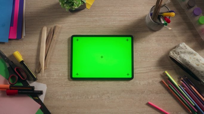 从上到下放大的平板电脑与模拟绿色屏幕显示视图。一个设备水平躺在一个创意儿童房间的桌子上的电影镜头。在
