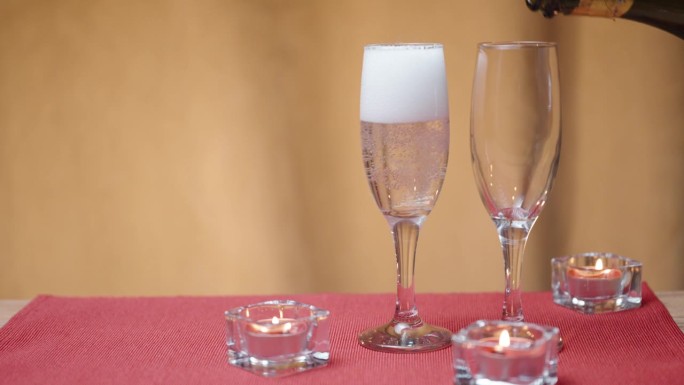 浪漫的两人桌。我把香槟酒倒进两个杯子里。红色桌子上的蜡烛。
