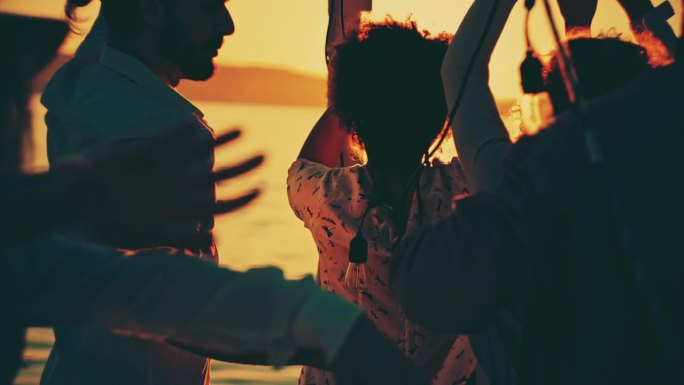 一群朋友在日落时分在船甲板上跳舞的慢镜头。