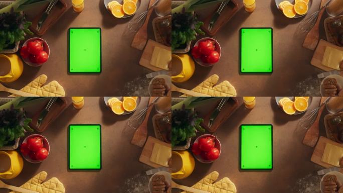 一个平板电脑与模拟绿色屏幕显示的自上而下的视图。一个设备垂直躺在厨房桌子上的静态镜头。在线烹饪和食物