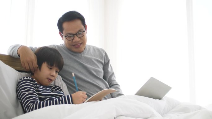 单亲父亲一边帮儿子做作业，一边用笔记本电脑