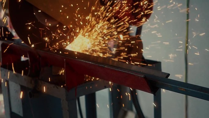 工人在生产车间用圆锯切割金属通道，火花飞溅。