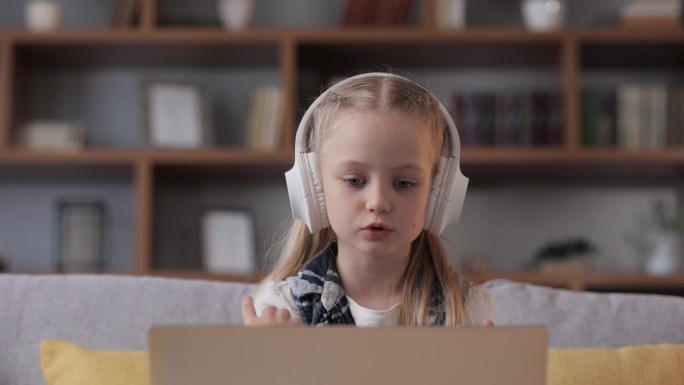 小学生戴着耳机上网上课，与老师视频通话，答疑解惑，核对知识。可爱的孩子在家里用笔记本电脑学习。远程学