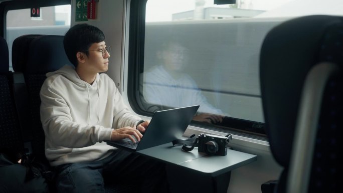 一个亚洲商人坐在火车上，然后把注意力集中在笔记本电脑上，开始工作。