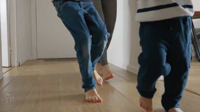一位母亲和两个男孩在家里的木地板上奔跑的慢镜头。家庭纽带，快乐和玩耍