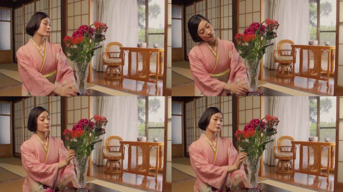 一位美丽的日本女性的肖像，穿着粉红色的和服，坐在榻榻米地板上，欣赏着一个装有彩色花束的花瓶。年轻女子