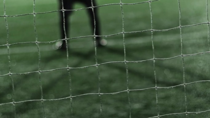 在晚上的足球比赛中，守门员的双腿站在球门上。专注足球网。摇晃的手持镜头