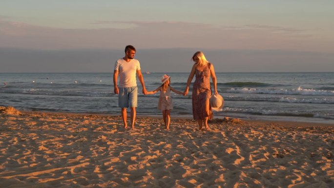 日落时分，一家人带着孩子在海边的沙滩上散步。夏天的旅行